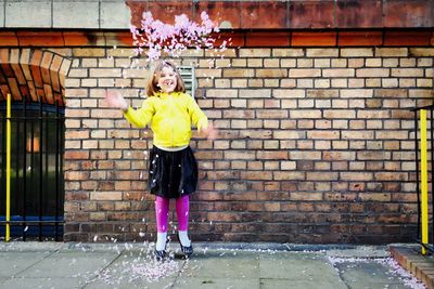 Full length portrait of woman standing against yellow wall