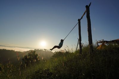 Silhouette man on wooden post on field against sky during sunset