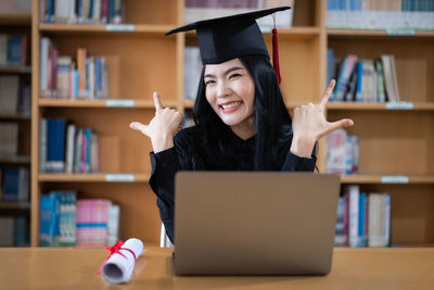 Close-up of smiling young woman wearing graduation gown in library