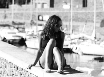 Mid adult woman sitting on retaining wall at harbor during sunny day