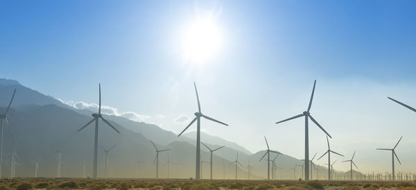 Windmills on field against sky on sunny day