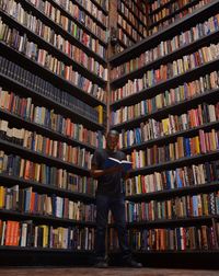 Low angle view of man reading book while standing by bookshelves in library