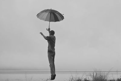 Rear view of man standing at shore against sky