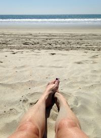 Low section of man on beach against sky