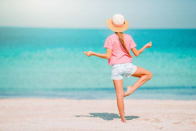 Rear view of girl standing on beach against sky