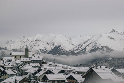 Scenic view of snowcapped mountains in front 8of houses against clear sky during winter