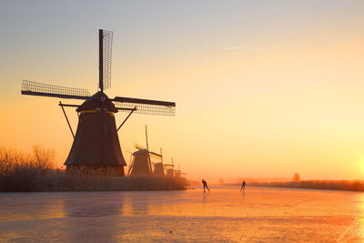Silhouette of windmill by sea against sky during sunset