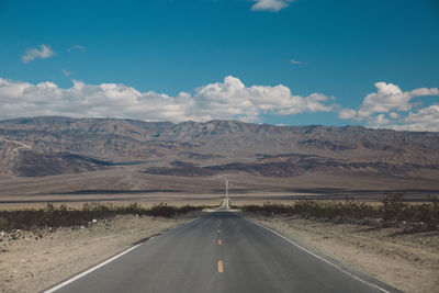 Empty road amidst field against sky