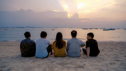 Rear view of people sitting on sand at beach during sunset