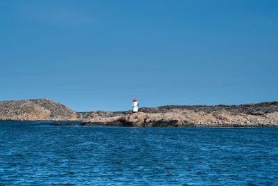 Lighthouse by sea against clear blue sky