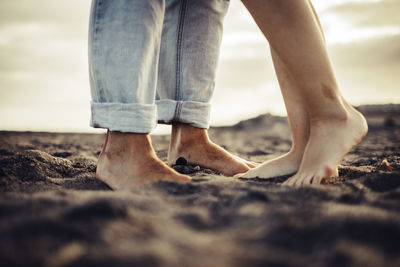 Low section of couple standing on sand at beach