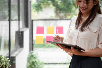 Midsection of woman holding smart phone standing at home