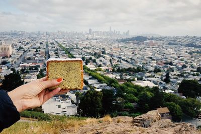 Cropped hand holding bread against city