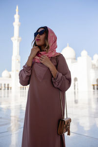 Woman in traditional clothing standing against mosque