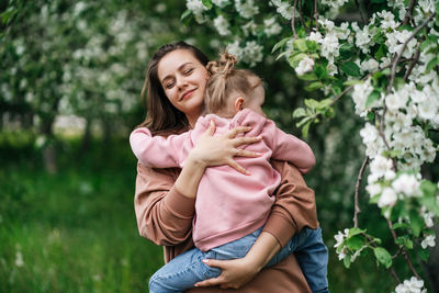 Young mother with her daughter in her arms in a blooming apple orchard