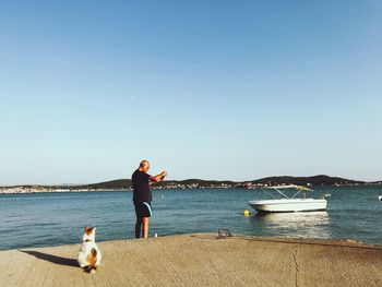 Cat sitting on pier by man adjusting fishing rod