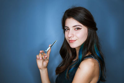Cute young woman with brunette with blue strands of hair holding scissors near