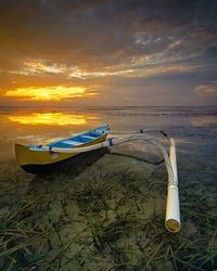 Boat moored on beach against sky during sunset