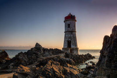 Lighthouse by sea against sky during sunset