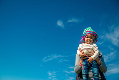 Mother carrying daughter against blue sky