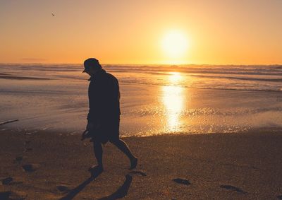 Silhouette man standing on beach against sky during sunset