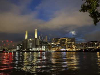 Illuminated city by river against sky