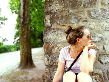 Young woman looking up while sitting on tree trunk