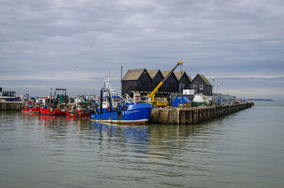 Fishing boats moored on sea by buildings against sky