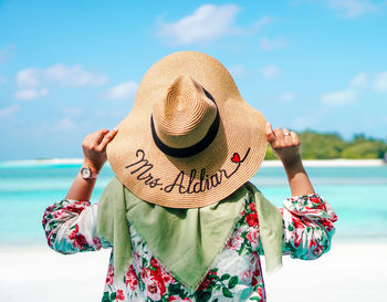 Midsection of person holding hat against sea