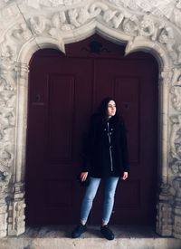 Full length portrait of woman standing against door