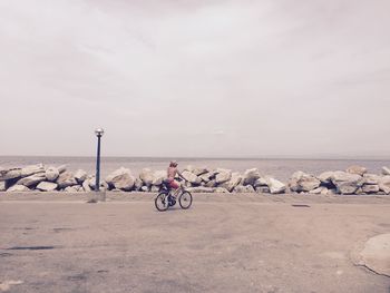 Woman riding bicycle at beach against sky