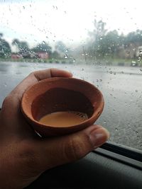 Close-up of hand holding wet glass window in rainy season