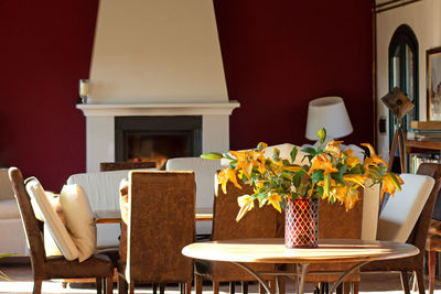 Interior with table and flowers in vase, chairs and dining table, fireplace. 