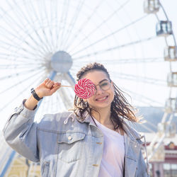 Portrait of smiling young woman holding lollipop with ferries wheel background