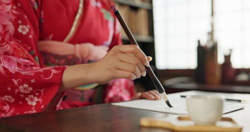 Midsection of woman writing in book at table