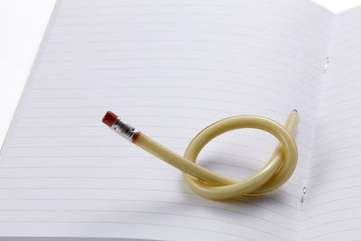 Close-up of knotted pencil and book against white background