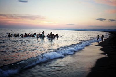 People on beach against sky during sunset