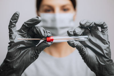 Close-up of doctor wearing mask holding test tube against gray background