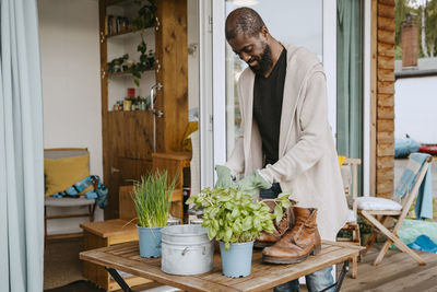 Mature man wearing cardigan doing gardening at table while standing on porch