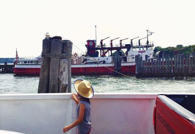 Woman standing on boat moored at harbor against clear sky