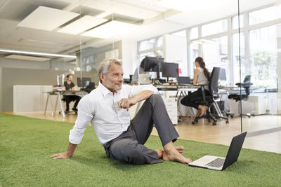 Businessman sitting on carpet in office with laptop