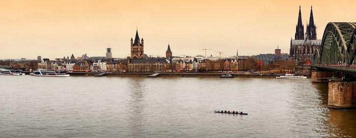 Boats moored in river by buildings against sky