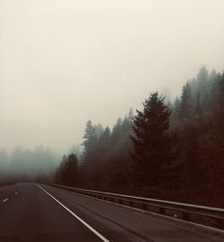 Road by trees against sky during winter