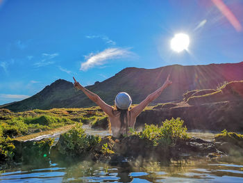 Rear view of woman with arms raised at hot spring against mountain