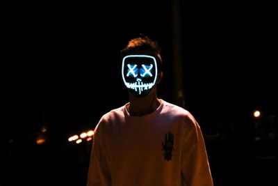 Portrait of man standing against illuminated sign at night