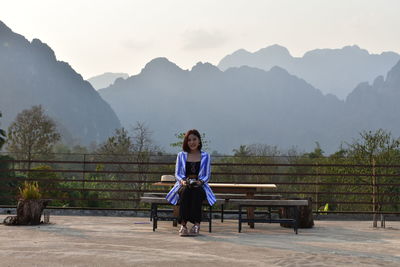 Portrait of man sitting on bench against mountains