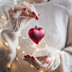 Midsection of woman with illuminated string lights holding red heart shape bauble during christmas