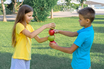 Teenage children play with apples in the park.