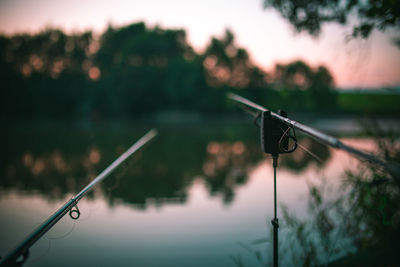 Close-up of fishing rods by lake during sunset