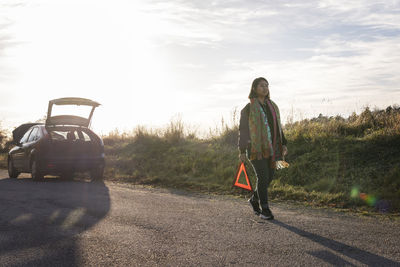 Woman on road holding warning triangle